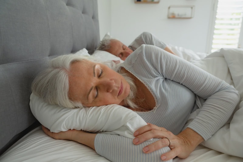 3 Health Benefits for Using Your AC While Sleeping. Senior couple sleeping in their bed.