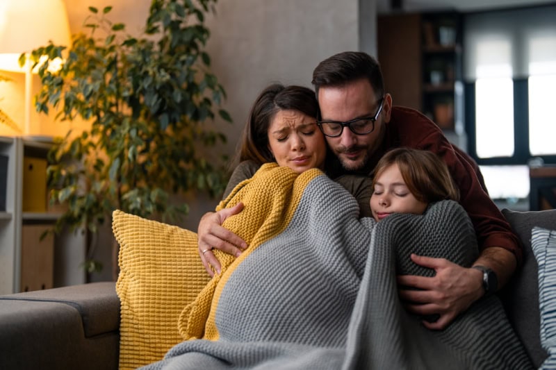 Why Isn’t My Furnace Heating My Entire Home? Photo of a family of three huddled together freezing under blankets to stay warm.